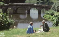 A couple of visitors sitting on a bank by the lake at Stourhead, Wiltshire