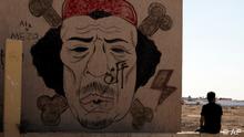 Líbio senta-se junto a graffiti de Kadhafi, em Bengazi, no dia da morte do líder líbio, a 20 de Outubro
