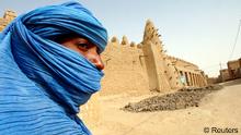 A Tuareg nomad stands near a 13th century mosque in Timbuktu in this March 19, 2004 file photo. Just as Timbuktu with its exotic staccato name is part of the lore of the Sahara, this same mystery cloaks the Tuaregs, those blue-robed desert marauders who have peopled adventure stories and Hollywood films for years. But there is nothing fictional about the rebels of the National Movement for the Liberation of Azawad (MNLA) who charged into Timbuktu on Sunday to plant their yellow, green, red and black flag in the city to claim it as part of a homeland covering an area of northern Mali the size of France. To match story MALI-TIMBUKTU/MYTH REUTERS/Luc Gnago/Files (MALI - Tags: POLITICS CIVIL UNREST RELIGION)