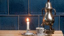 Eine Dröppelminna, darunter eine Kaffeetasse, daneben eine brennende Kerze

