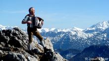 Josef Ecker mit Ziehharmonika auf einer Bergspitze.

